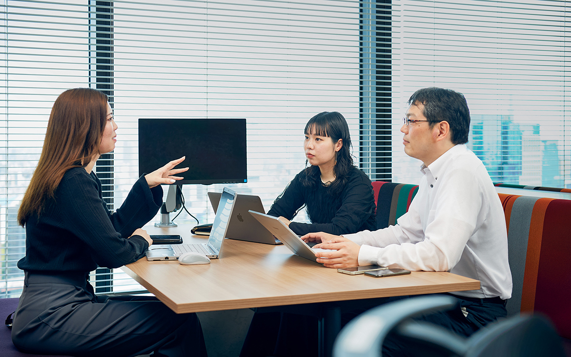 窓際の席で打ち合わせをする3人の社員